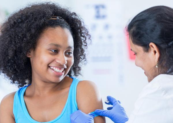 A teenage girl smiles after receiving a vaccine.