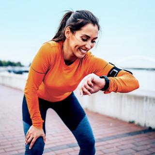 A woman takes a break while going for a run to check her smartwatch.