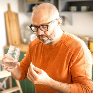 A man holds a glass of water in one hand and a pill in the other.