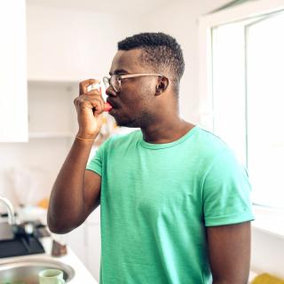 A young man uses his inhaler in his kitchen.